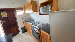 A compact kitchen with wooden cabinets, a stove, a microwave, and a refrigerator. - Suntide Cabanas ground floor studio apartment, Margate beach (Margate)