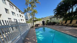 A swimming pool with a white fence, palm trees, and lounge chairs. - Suntide Cabanas ground floor studio apartment, Margate beach (Margate)
