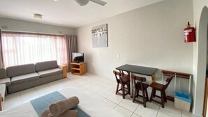 A living room with a sofa, TV, dining table, chairs, and a fire extinguisher. - Suntide Cabanas ground floor studio apartment, Margate beach (Margate)