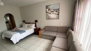 A bedroom with a bed, a sofa, a painting on the wall, and a window with curtains. - Suntide Cabanas ground floor studio apartment, Margate beach (Margate)