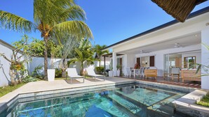 A modern house with a clear swimming pool, outdoor seating, and tropical plants.