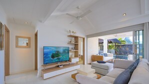 A modern living room with a flat-screen TV, a ceiling fan, and a large window overlooking a pool area.
