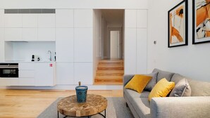 A modern apartment with a kitchen, a living area with a sofa and cushions, and a staircase leading to another room.