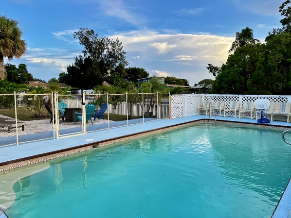 A swimming pool with a white fence, blue lounge chairs, and a clear sky.