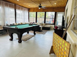 A pool table in a room with a ceiling fan, large windows, and a view of the outside.