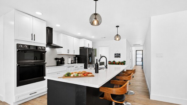 A modern kitchen with white cabinetry, a central island with bar stools, a black stove, and pendant lighting. - Bahama Mama at Lake Granbury (Granbury)