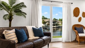A brown leather sofa with blue and beige cushions, a wicker chair, a large potted plant, and a view of a body of water through a glass door. - Bahama Mama at Lake Granbury (Granbury)