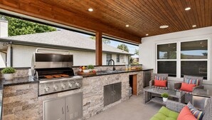 An outdoor kitchen with a grill, stone countertops, and a seating area with wicker furniture. - Bahama Mama at Lake Granbury (Granbury)