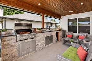 An outdoor kitchen with a grill, stone countertops, and a seating area with wicker furniture.