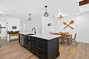 A modern kitchen with a central island, black cabinetry, and a dining area with wicker chairs.