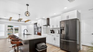 A modern kitchen with a central island, stainless steel appliances, and wooden bar stools. - Bahama Mama at Lake Granbury (Granbury)