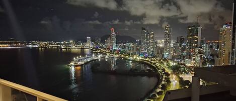 A nighttime cityscape with a waterfront, illuminated buildings, and a curved road along the water.
