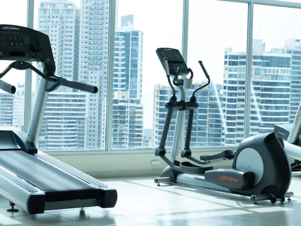 Une salle de sport intérieure équipée de machines de cardio et dotée d’une grande fenêtre offrant une vue sur la ville.