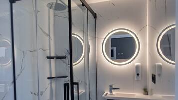 Un baño moderno con ducha de vidrio, tocador con espejo y pared de mármol.