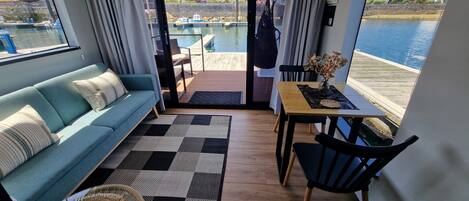 A modern living room with a sofa, a dining table, and a view of a marina.
