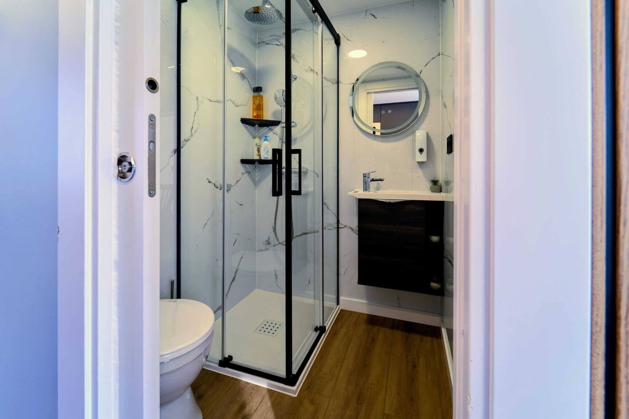 Une salle de bain moderne avec une douche en verre, des toilettes, un lavabo avec un miroir et des murs en marbre.