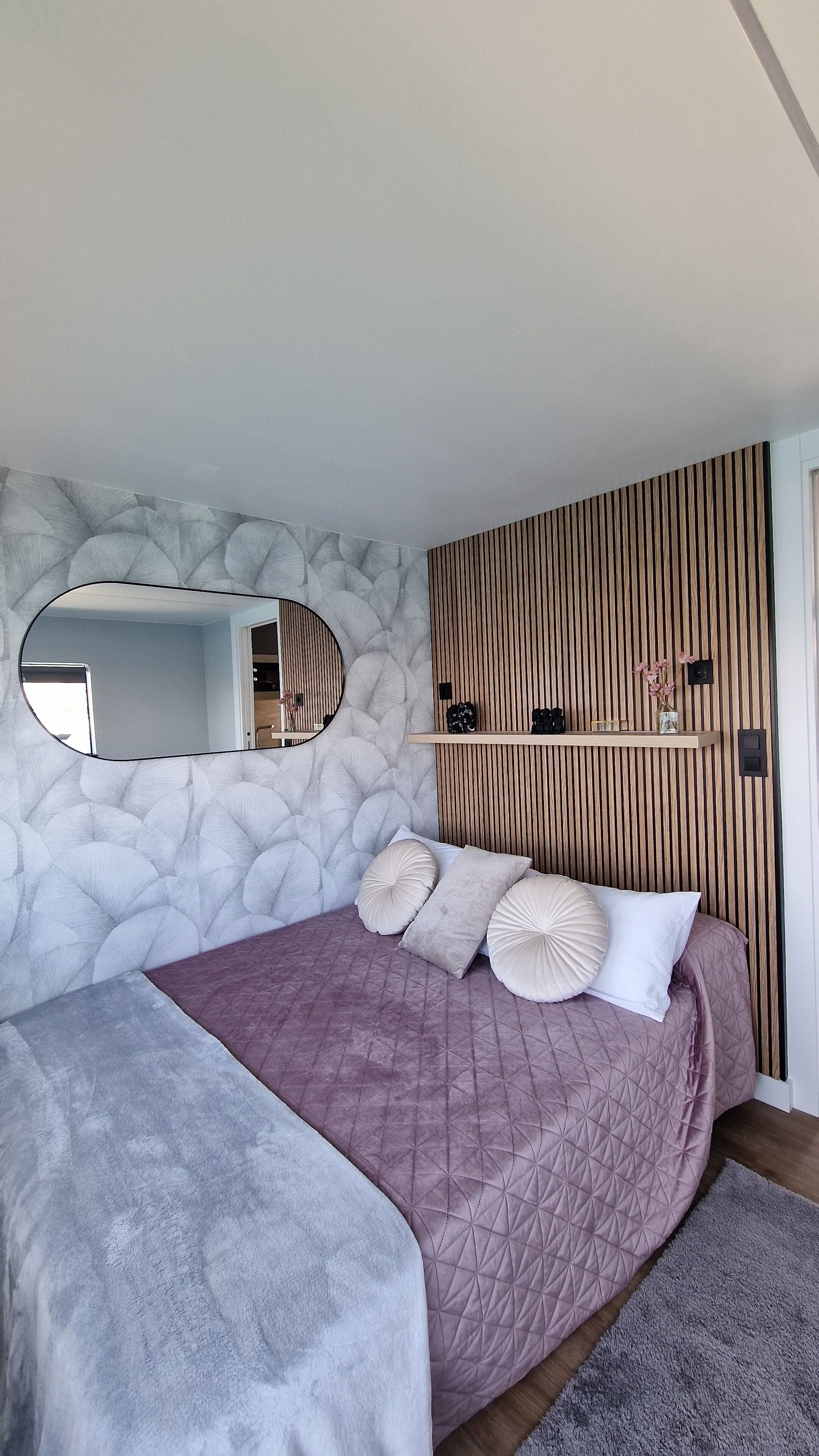 Ein Schlafzimmer mit einem Bett, einem Spiegel, einer Wand aus Holzverkleidung und einem Regal mit Gegenständen.