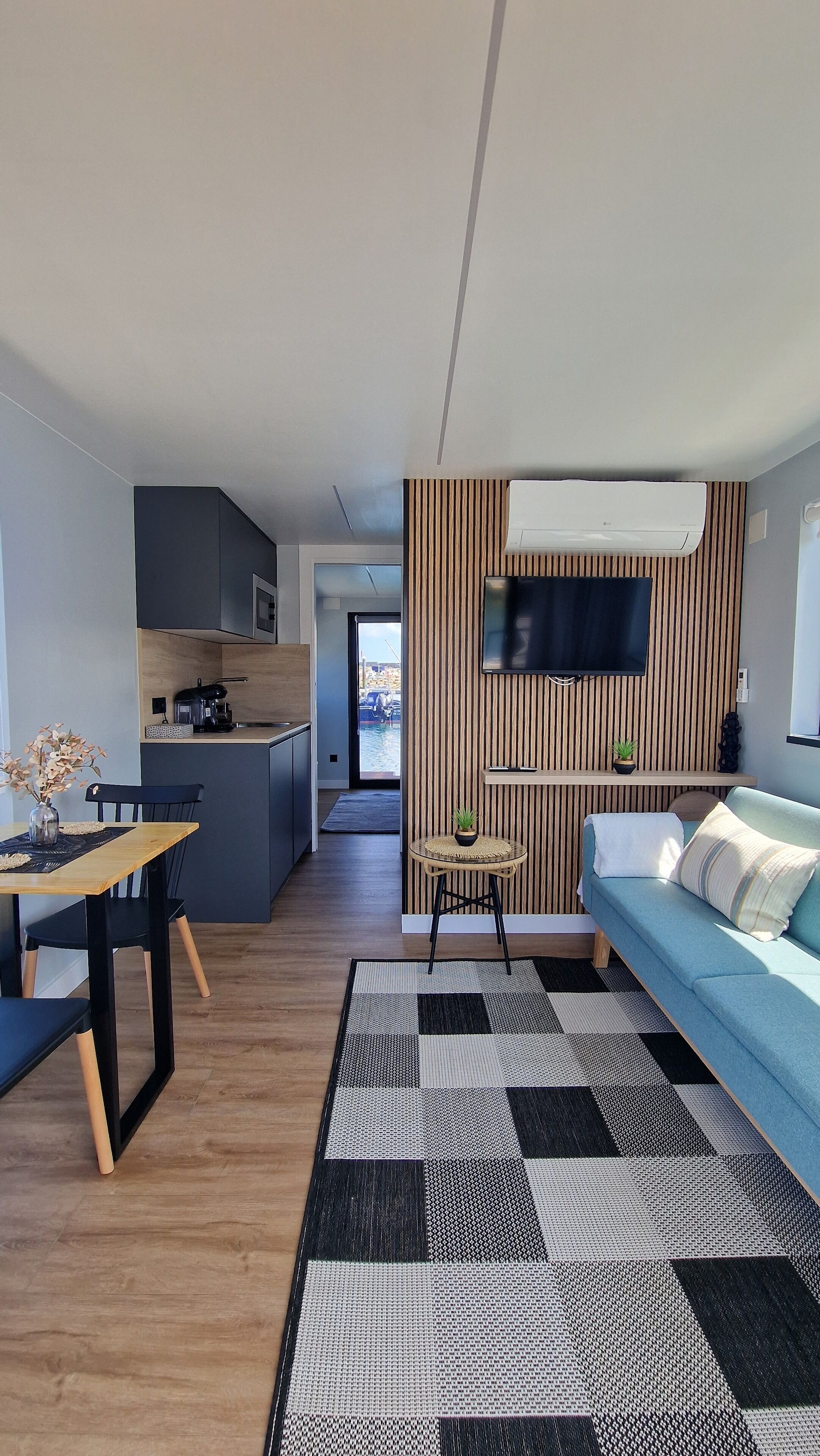 Un espace de vie moderne comprenant un coin repas, une cuisine et un téléviseur fixé sur un mur revêtu de panneaux en bois.
