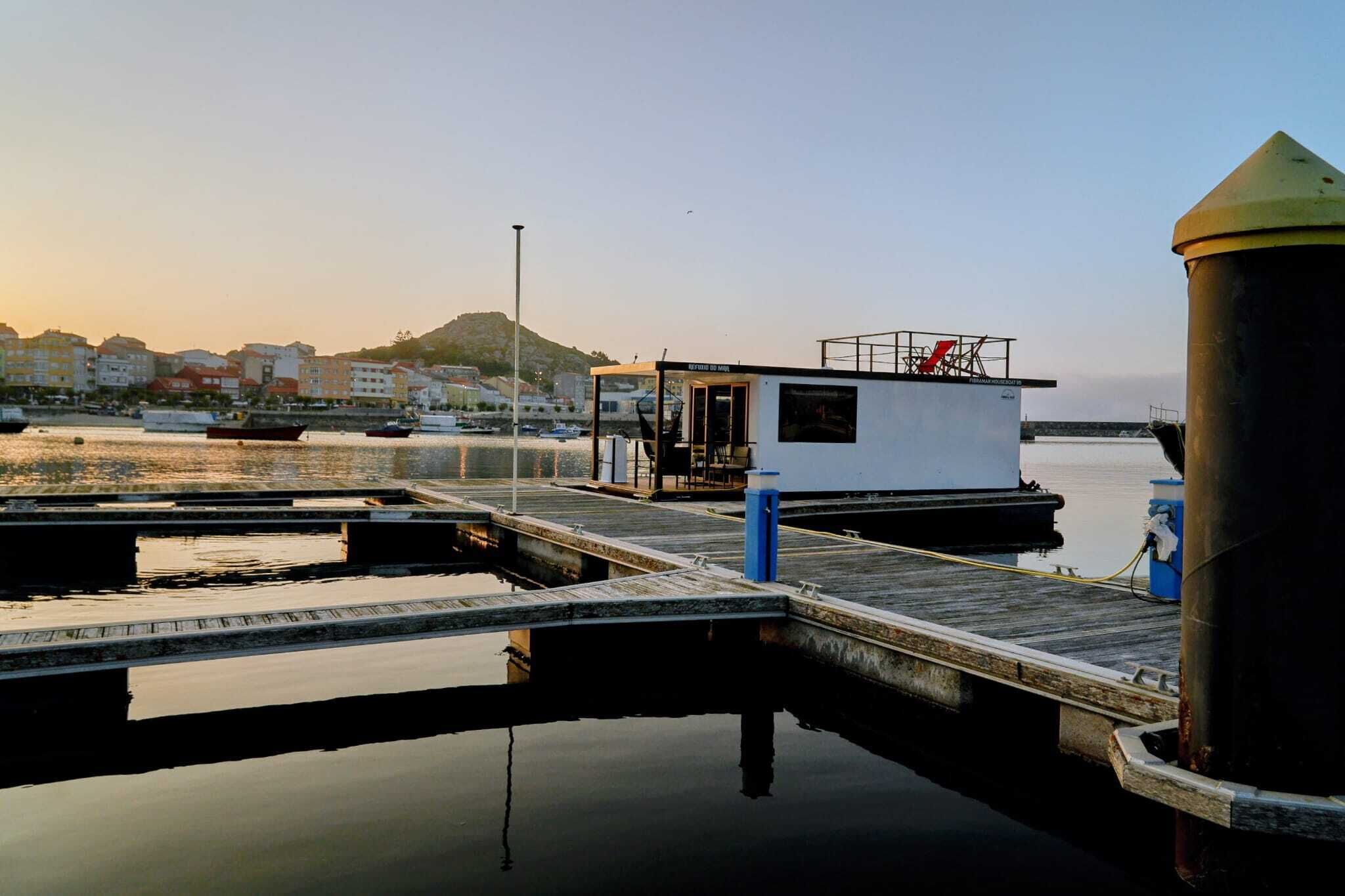 Un port de plaisance avec des bateaux amarrés, un petit bâtiment blanc avec un toit rouge et un grand réservoir cylindrique.
