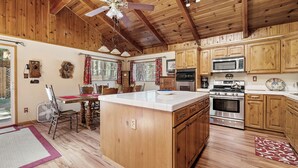 Una cocina con armarios de madera, una isla central, un microondas, un horno y una zona de comedor con una mesa y sillas.