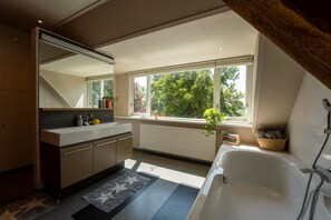A modern bathroom with a large window, a bathtub, and a sink with a mirror above it.