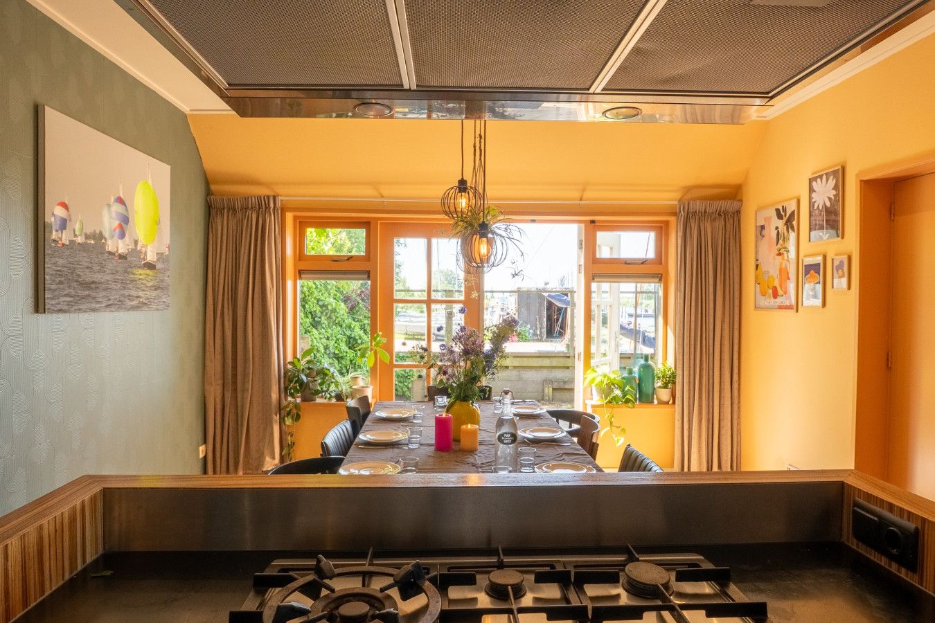 Comedor con una mesa dispuesta para cuatro, una estufa a gas al frente y ventanas grandes con cortinas.