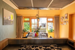 A dining area with a table set for four, a gas stove in the foreground, and large windows with curtains.