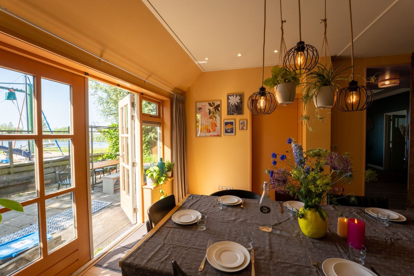 Comedor con una mesa preparada para cuatro personas, ventanas amplias y lámparas colgantes.