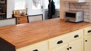 A kitchen with a wooden countertop, white cabinets, and a microwave.