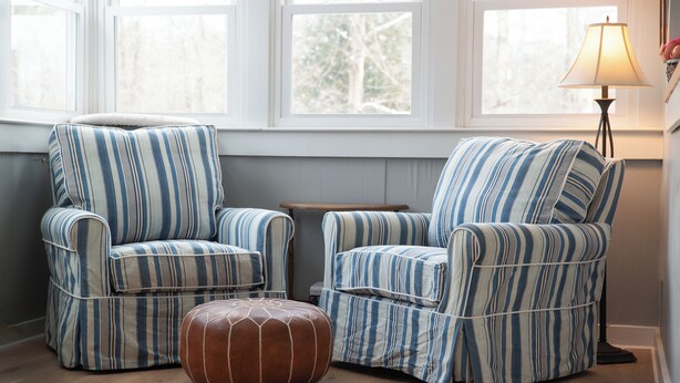 A room with two striped armchairs and a matching ottoman, a wooden side table, and a floor lamp.
