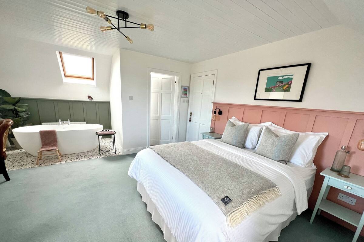Une chambre à coucher avec un grand lit, une table de chevet, une commode, une chaise, une baignoire et un luminaire au plafond.