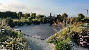 A paved area with a wooden structure, surrounded by various plants and shrubs.