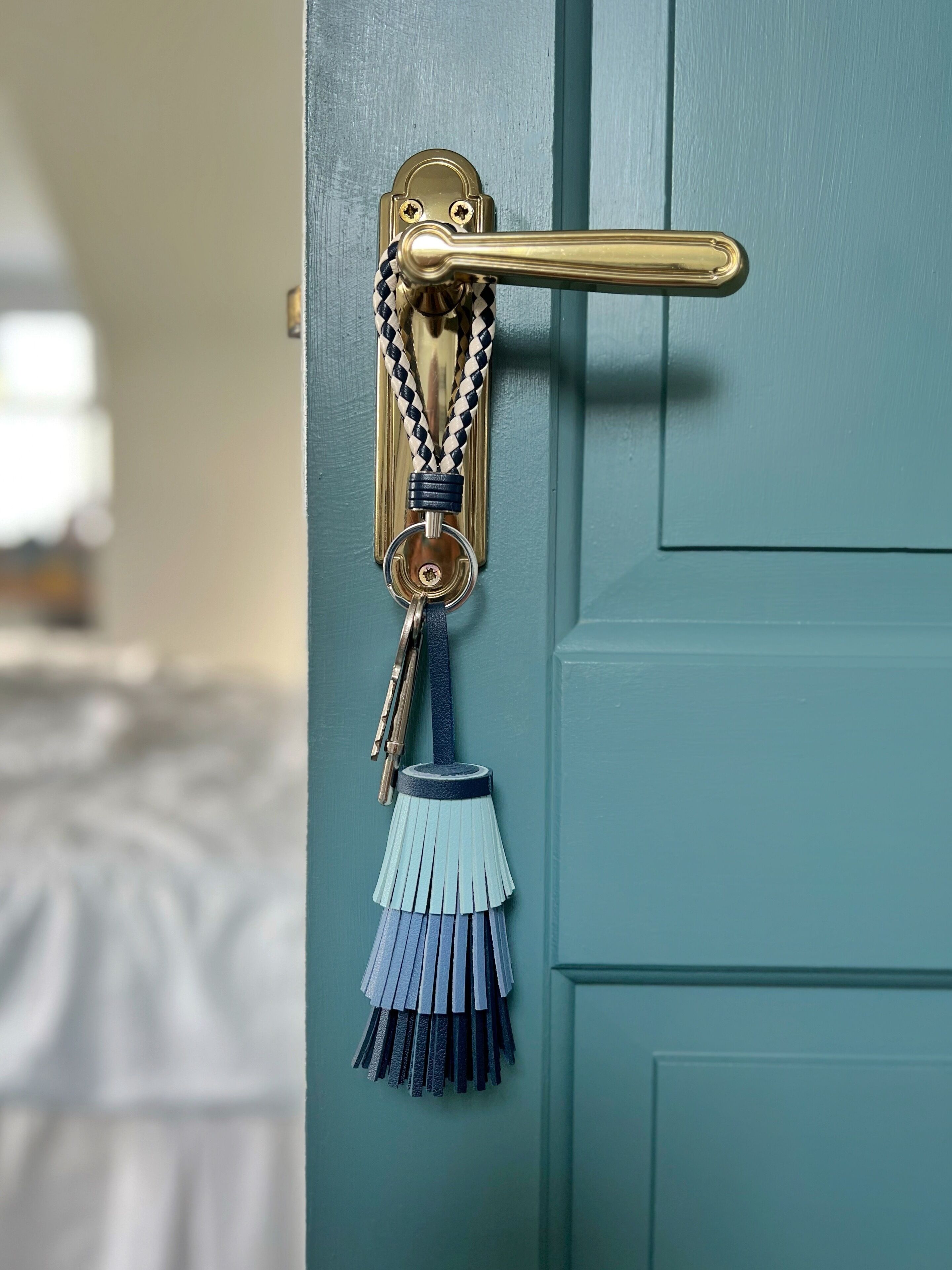 A door with a brass handle and a keychain with a braided rope and a blue tassel.