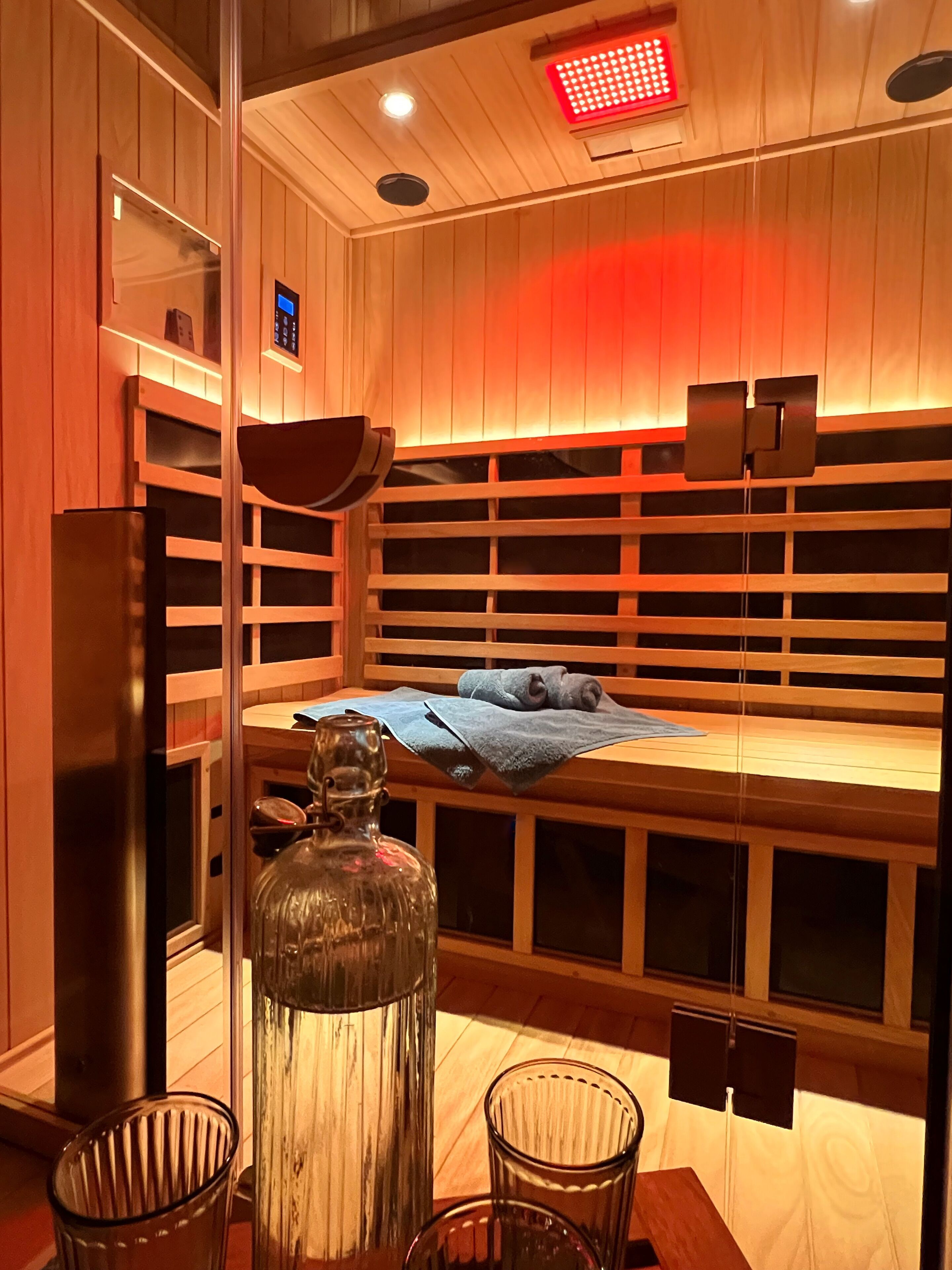 Ein Zimmer mit Holzbalkendecke, einem Bett mit blauer Decke, einer Glasflasche und einem kleinen Tisch mit Stühlen.
