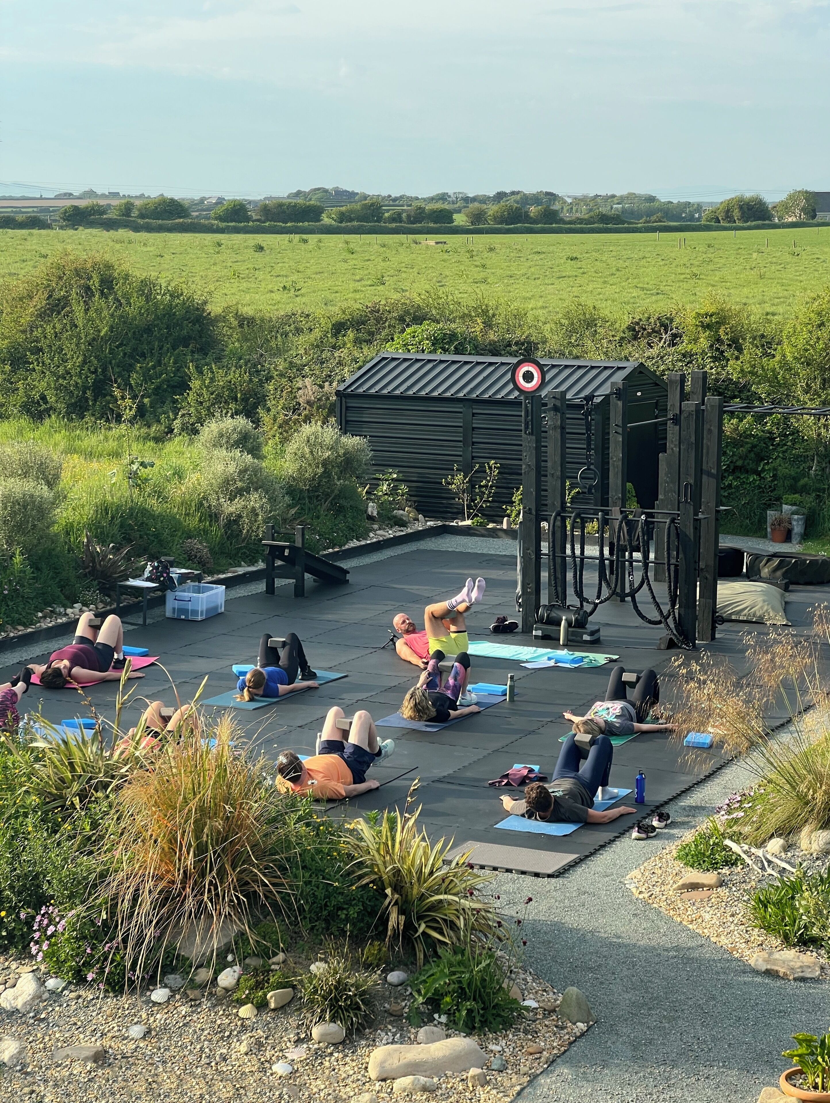 Clase de yoga al aire libre en una azotea con vistas a un campo verde y colinas al fondo.