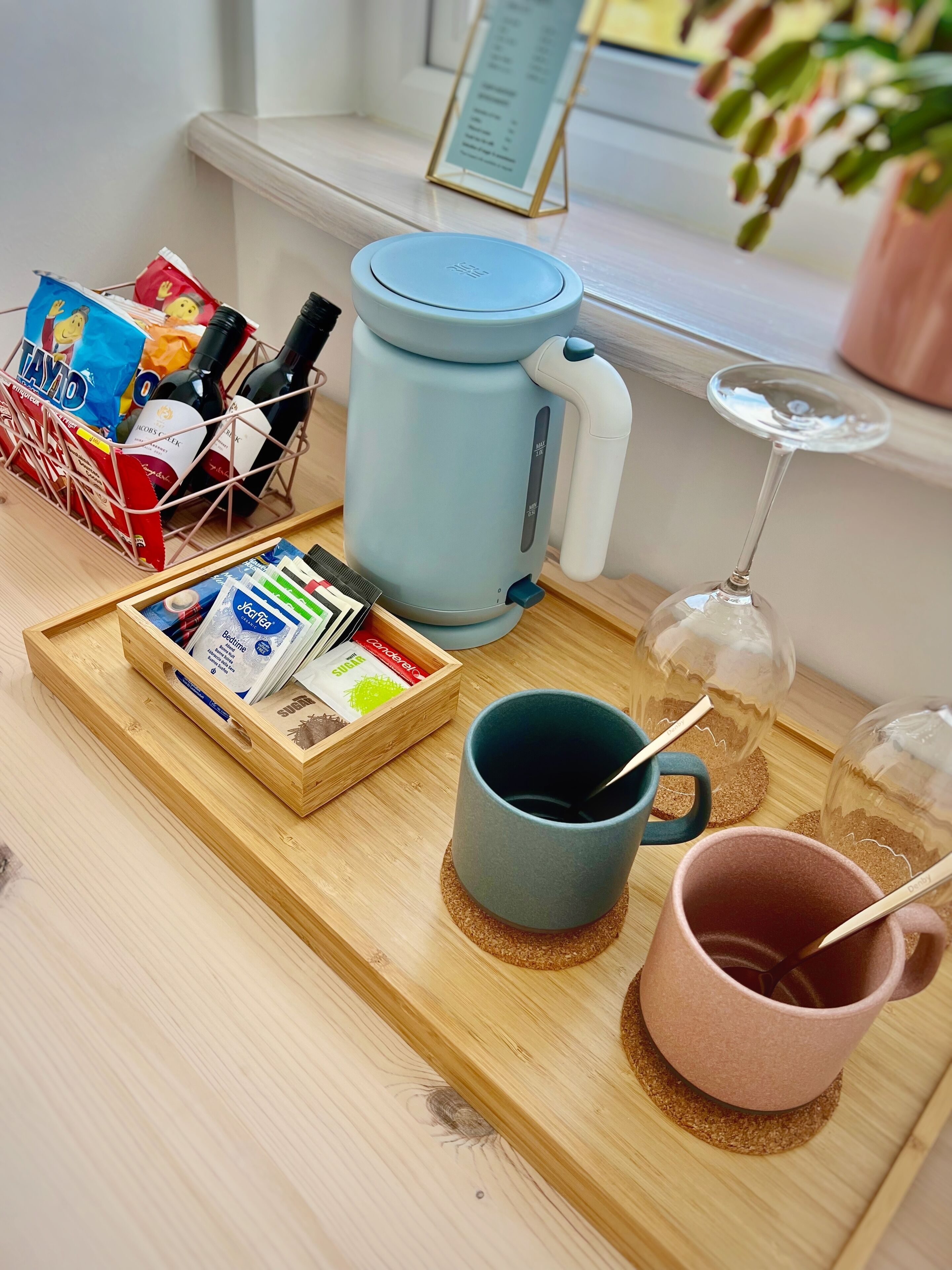 Una bandeja con una cafetera, una taza y una copa de vino sobre una mesa de madera.