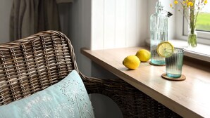 A wicker chair with a cushion, a wooden table with a glass pitcher, lemons, and a glass with a lemon slice. - Thistledown Lodge (Templetown)