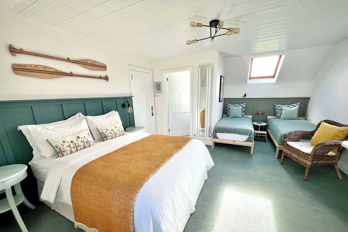 Une chambre à coucher avec un grand lit, un plus petit lit, une chaise, une table et un ventilateur de plafond.