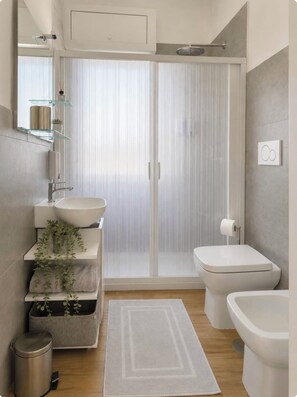 Une salle de bain moderne avec une douche à parois de verre, un lavabo avec un miroir au-dessus, des toilettes et un bidet.