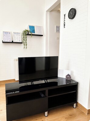 Ett svart TV-möblemang med en platt-TV, en hylla med en växt och en väggklocka.