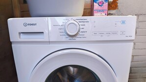 Lavadora blanca con panel de control, etiqueta que indica un descuento del 10% y una caja de detergente cerca.