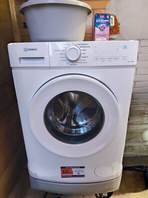 A white washing machine with a control panel, a label indicating a 10% discount, and a nearby detergent box.
