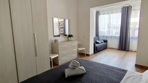 Un dormitorio moderno con cama, cómoda, silla y un ventanal con cortinas.