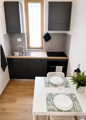 Ett kompakt kök med en diskho, skåp och en matplats med ett bord som är dukat för två personer.