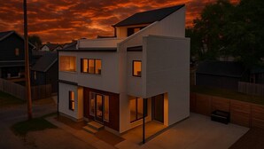 Une maison moderne à deux étages, dotée d’un toit plat, de grandes fenêtres et d’une porte d’entrée bien visible.