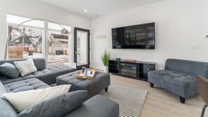 Un salon moderne avec un canapé d’angle gris, un téléviseur à écran plat fixé au mur et une petite table d’appoint avec un plateau.