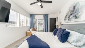 Une chambre moderne avec un grand lit, un ventilateur de plafond et une vue sur la ville par les fenêtres.