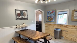 A kitchen with a wooden table and benches, a trash can, and two wall-mounted maps. - Quaint home with large yard, pet friendly, bike storage right off the trailhead (Lanesboro)