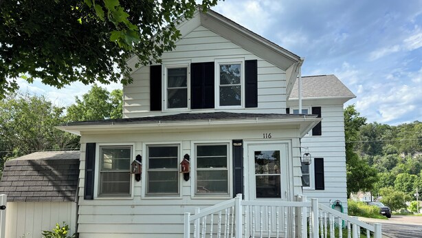 A two-story house with a white exterior, black shutters, and a white porch with a railing. - Quaint home with large yard, pet friendly, bike storage right off the trailhead (Lanesboro)