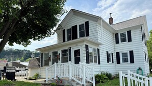 A two-story house with a white exterior, black shutters, and a white porch with a railing. - Quaint home with large yard, pet friendly, bike storage right off the trailhead (Lanesboro)